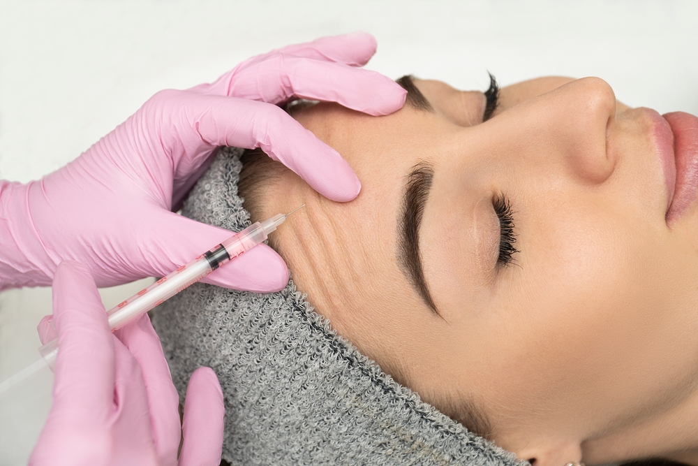 Mulher aplicando toxina botulínica em testa de paciente.